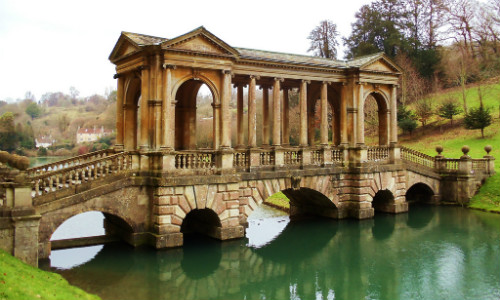The Palladian Bridge at Prior Park, with its graceful columns supporting its classically-inspired roof above, stretches across a small body of still water
