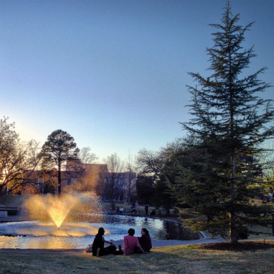 Students enjoy sitting by the Duck Pond as the last light of the day falls golden through the streaming waters of the fountain